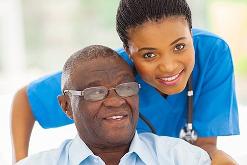 Elderly african american man with young nurse standing behind him smiling