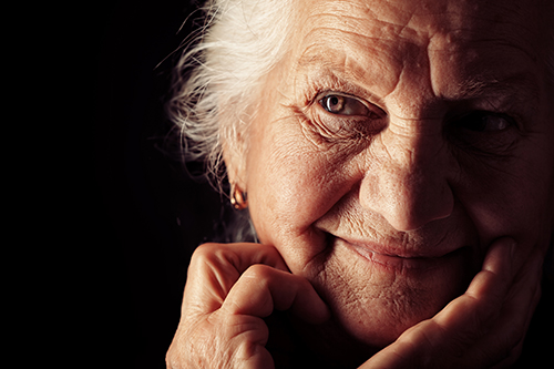 Close of elderly woman with her hand resting on her face with a dark background