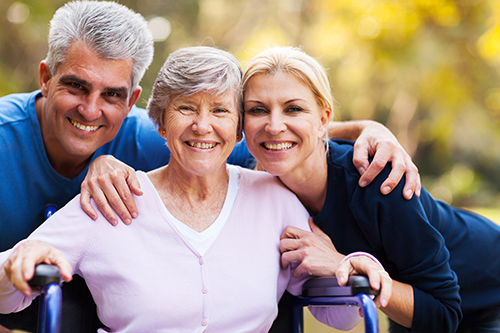 Elderly woman in wheelchair smiling with her husband and daughter on each side of her